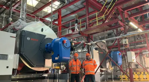 Two workers in orange safety gear stand in a large industrial facility, surrounded by red steel structures and Bosch machinery.