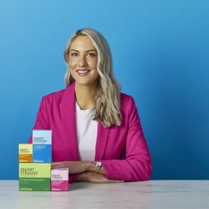 Dr. Megan Rossi holding a box of SMART STRAINS live bacteria supplements in a retail store aisle.