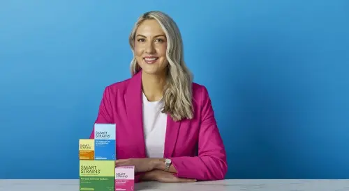 Dr. Megan Rossi holding a box of SMART STRAINS live bacteria supplements in a retail store aisle.