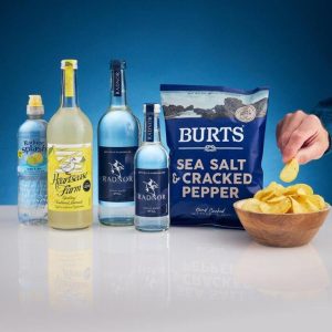 A bag of Burts hand-cooked potato chips placed next to a bottle of Radnor Hills spring water on a rustic wooden table.