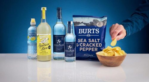 A bag of Burts hand-cooked potato chips placed next to a bottle of Radnor Hills spring water on a rustic wooden table.