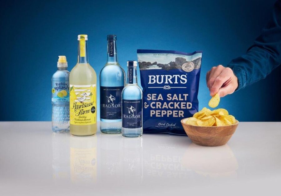 A bag of Burts hand-cooked potato chips placed next to a bottle of Radnor Hills spring water on a rustic wooden table.
