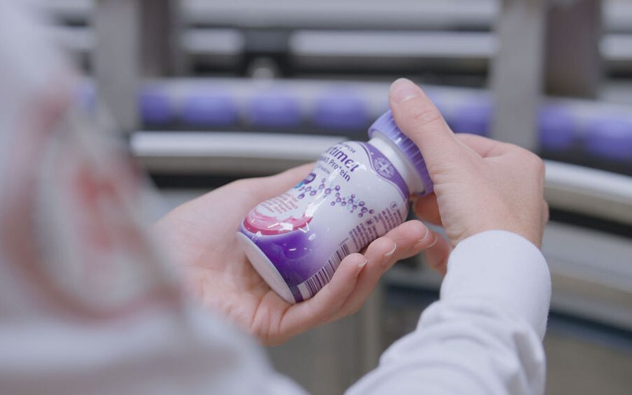 Worker inspecting a Fortimel medical nutrition bottle on Danone's Steenvoorde production line