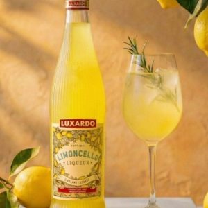A premium bottle of Luxardo Limoncello showing the new clear glass design with vertical fluting that catches the light, filled with a vibrant yellow lemon liqueur.