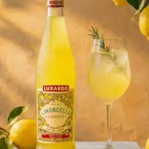 A premium bottle of Luxardo Limoncello showing the new clear glass design with vertical fluting that catches the light, filled with a vibrant yellow lemon liqueur.