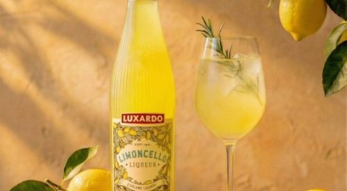 A premium bottle of Luxardo Limoncello showing the new clear glass design with vertical fluting that catches the light, filled with a vibrant yellow lemon liqueur.