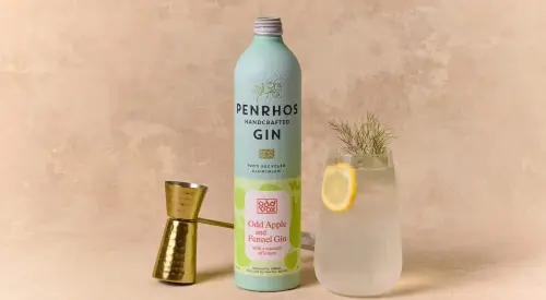 A bottle of Penrhos handcrafted gin beside a jigger and a glass of gin with a lemon slice and a sprig of herb