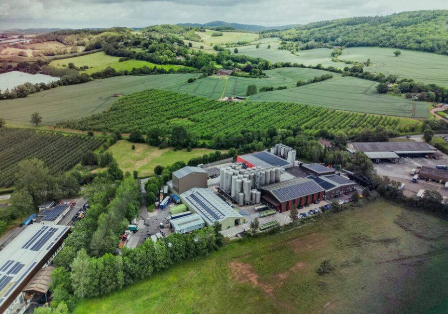 An aerial view of the Bevisol processing facility in Ledbury, Herefordshire, showcasing industrial storage tanks, solar-panelled roofing, and surrounding agricultural farmland