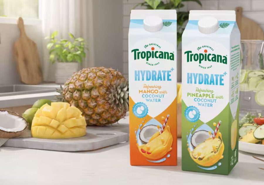Two cartons of Tropicana Hydrate plus coconut water drink in Mango and Pineapple flavors on a bright kitchen counter next to a fresh whole pineapple, sliced mango, and coconut
